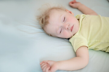 Wall Mural - small child sleeps with arms outstretched. girl with blond hair in yellow bodysuit. Concept healthy sleep