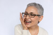 Close-up of senior woman laughing and touching face over white background. Mature Caucasian woman wearing eyeglasses and white jumper looking away and smiling. Happiness concept