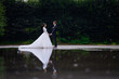 Young loving brides couple holding hands standing near lake looking at each other. Beautiful bride woman in puffy dress with man husband in elegant suit. Family. Wedding day celebration.