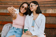 © Drobot Dean - Two asian women taking selfie photo on cellphone while sitting on bench