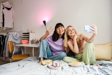 Wall Mural - Two multiracial girls making fun while taking selfie on mobile phone