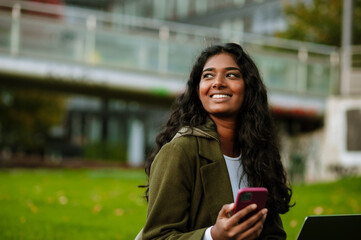 young woman using laptop and cellphone while sitting on grass in park