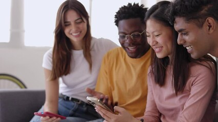 Young group of diverse friends sitting on sofa using mobile phone. Smiling multiracial teenage people laughing having fun together watching funny social media video content on smart phone at home