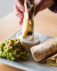 Wall Mural - Woman dipping a Garden quesadilla in white sauce with a side of bacon guacamole on the plate