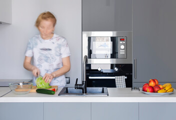 A woman cooking vegetarian food in a modern kitchen in gray tones. Blurry motion