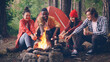 multiracial group of tourists is cooking food roasting marshmallow on open fire sitting in forest in circle and smiling. Hiking, healthy lifestyle and youth concept.