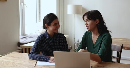 Wall Mural - Young smiling Indian woman listen to colleague makes speech, talking about on-line project seated together at desk with laptop, working at workplace, share business vision looking friendly. Mentoring.