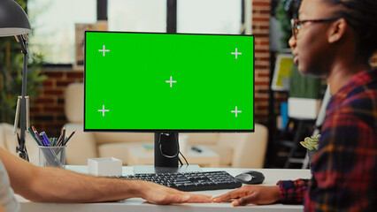 Multiethnic team working on computer with greenscreen at home, using monitor to examine isolated display and blank copyspace template. Analyzing mockup background on desktop screen.