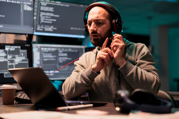 Software developer writing source code to create new user interface, programming html script and testing headset microphone. Working on developing system with multiple screens at night.