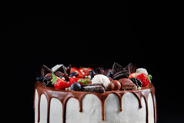 Wall Mural - Birthday cake on dark background with copy space. Close up of cake decorated with fresh berries and chocolate sweets on dark background. Delicious dessert for party