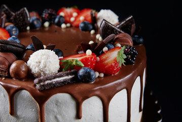 Wall Mural - Birthday cake on dark background. Close up of cake decorated with fresh berries and chocolate sweets on dark background. Delicious dessert for party