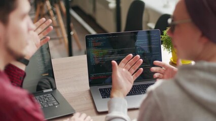Two hipster coworkers sharing ideas about project sitting with laptops in spacious open space office. Developers discuss application program code. Coder and manager consulting software architecture.