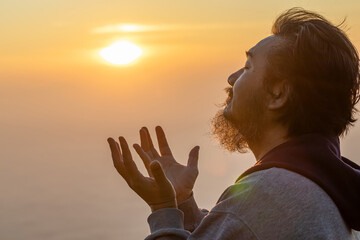 Portrait of young adult male with beard praying for thank god golden sunset background.