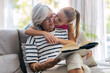 © Westend61 - Girl kissing grandmother reading book sitting on sofa at home