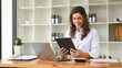 © bongkarn - Beautiful millennial Caucasian businesswoman using her tablet at her office desk.