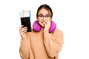 Wall Mural - Young caucasian woman with inflatable travel pillow holding passport isolated on green chroma background biting fingernails, nervous and very anxious.