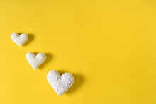 Three White Knitted Hearts On A Yellow Background. The Layout Of A Valentine's Day Greeting Card With Hearts On A Pink Background. A Place To Copy. Flat Position, Top View.