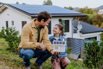 Wall Mural - Little girl with her dad holding paper model of house with solar panels, explaining how it works.Alternative energy, saving resources and sustainable lifestyle concept.