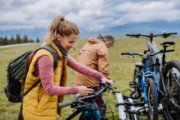 Young family preparing for bicycle ride in nature, putting off bicycles from car racks. Healthy lifestyle concept.