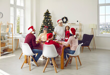 Family Celebrating Christmas. Older Family Member Makes Toast During Traditional Festive Family Christmas Dinner. Multi-generational Family In Santa Hats Gathered Together At Festive Table At Home.
