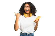 Young African American Woman Listening To Music With Yellow Headphones Isolated Points With Thumb Finger Away, Laughing And Carefree.