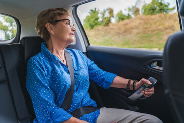 Beautiful happy senior woman in a blue blouse in the passenger seat in a car enjoying a trip