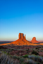 Monument Valley Famous Buttes Vertical View At Colorful Red Sunset In Arizona With Orange Rocks Formations And Blue Sky With East And West Mittens Shapes