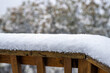 Macro closeup of snow powder covering wooden deck railing in winter with snowing falling snowflakes in Colorado