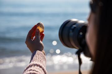 Beautiful woman taking a picture of a sea shell holding it with her hand