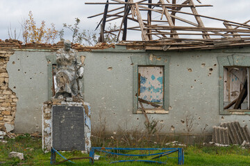 War in Ukraine. 2022 Russian invasion of Ukraine. Countryside. Monument to a soldier of the Second World War damaged by shelling against the background of a destroyed house