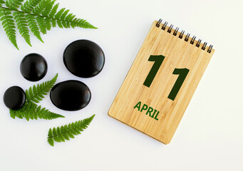 Wall Mural - April 11. 11th day of the month, calendar date. Notepad, black stones, green leaves. Spring month, the concept of the day of year