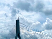 Aerial View Of The Tower Of Suspension Bridge With Numerous Cables On Blue Cloudy Sky Background