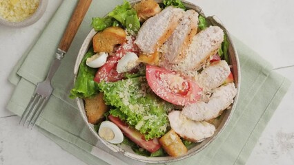 Wall Mural - Top view of Caesar salad in a plate with fork. Healthy salad made of chicken fillet, lettuce, tomatoes, quail eggs, croutons, parmesan cheese in a plate on white background