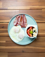 Sticker - Closeup of delicious breakfast with fried eggs and bacon slices with fruit salad on a wooden table