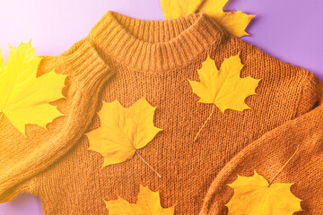 Wall Mural - Autumn concept, flat lay - brown knitted sweater and yellow autumn maple leaves on lilac paper, close-up