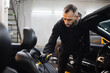 © sofiko14 - Car detailing concept. Brush cleaning of the car interior, front seat. Young man in black wear and protective gloves, cleaning car seat with soft brush and foam. Selected focus.
