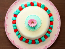 Cake With White Fondant, A Light Pink Daisy In The Center, Green And Red Accents On A Light Pink Plate