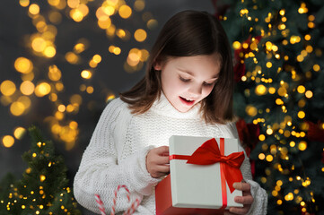 Merry Christmas and Happy New Year 2023. Happy girl opens gift on background of lights