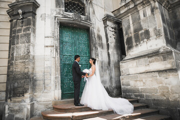 Wall Mural - Wedding photo shooting. Bride and bridegroom walking in the city. Married couple embracing and looking at each other. Holding bouquet