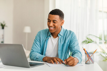 Wall Mural - Glad handsome young african american man manager in casual use computer for work, study, making notes