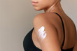 A white thick smear of moisturizing cream on the body of young caucasian tanned woman isolated on a gray background. Skin care