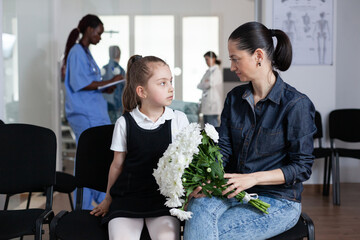 Wall Mural - Mom, daughter waiting to see hospitalized family member in hospital reception. Girl, young woman in hospital visiting area. Relatives bringing flowers to hospital patient.