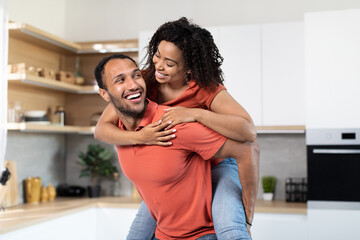 Satisfied young black male in red t-shirt holding woman on back, have fun, enjoy spare time