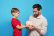 © New Africa - Father and his son with ceramic piggy bank on light blue background