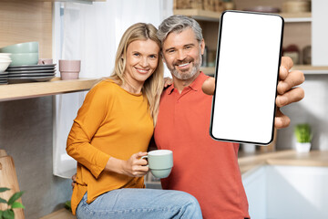 Romantic middle aged couple drinking coffee, showing cell phone, mockup