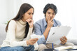 © KMPZZZ - Stressed financial owe asian young couple love hand in holding bills, sitting on sofa together, stressed and confused by calculate expense, mortgage or loan. Debt, bankrupt or bankruptcy people.