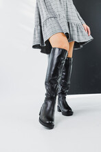 Slender female legs in black winter leather boots. Fashionable women's high boots. Women's leather shoes.