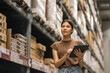 © Chanakon - Young female manager worker checklist manage parcel box product in warehouse. Asian woman supervisor using tablet working at store industry. Logistic import export concept.