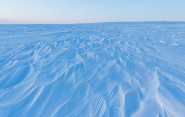 Wall Mural - Winter arctic landscape. Snow-covered tundra. On the surface of the snow, there are sastrugi (patterns formed by erosion of snow by wind). Cold frosty weather. The harsh climate of the polar region.