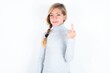 beautiful caucasian teen girl wearing gray turtleneck sweater over white wall shows middle finger bad sign asks not to bother. Provocation and rude attitude.
